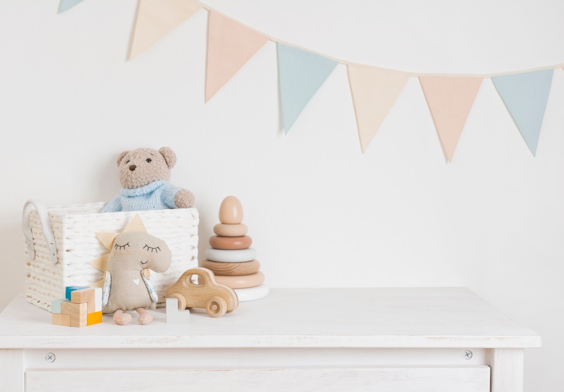 Kinderzimmer mit weißem Schrank, Stoffkorb mit Teddybär, Holzspielzeug und Wimpelkette an der Wand
